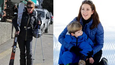 "Two women on a ski trip; one carries gear, another sits in the snow with a child."