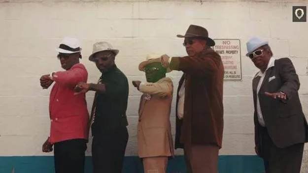 Elderly men dressed in colorful suits, fedoras, and sunglasses striking a cool, synchronized pose against a white wall.