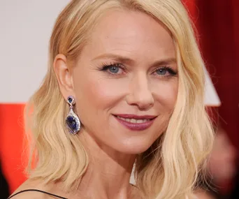 Blonde woman with waves, wearing blue gemstone earrings, smiling at an event.