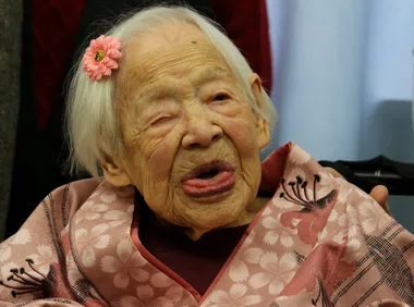 Elderly woman with floral hair accessory wearing a patterned kimono, showing a gentle expression.