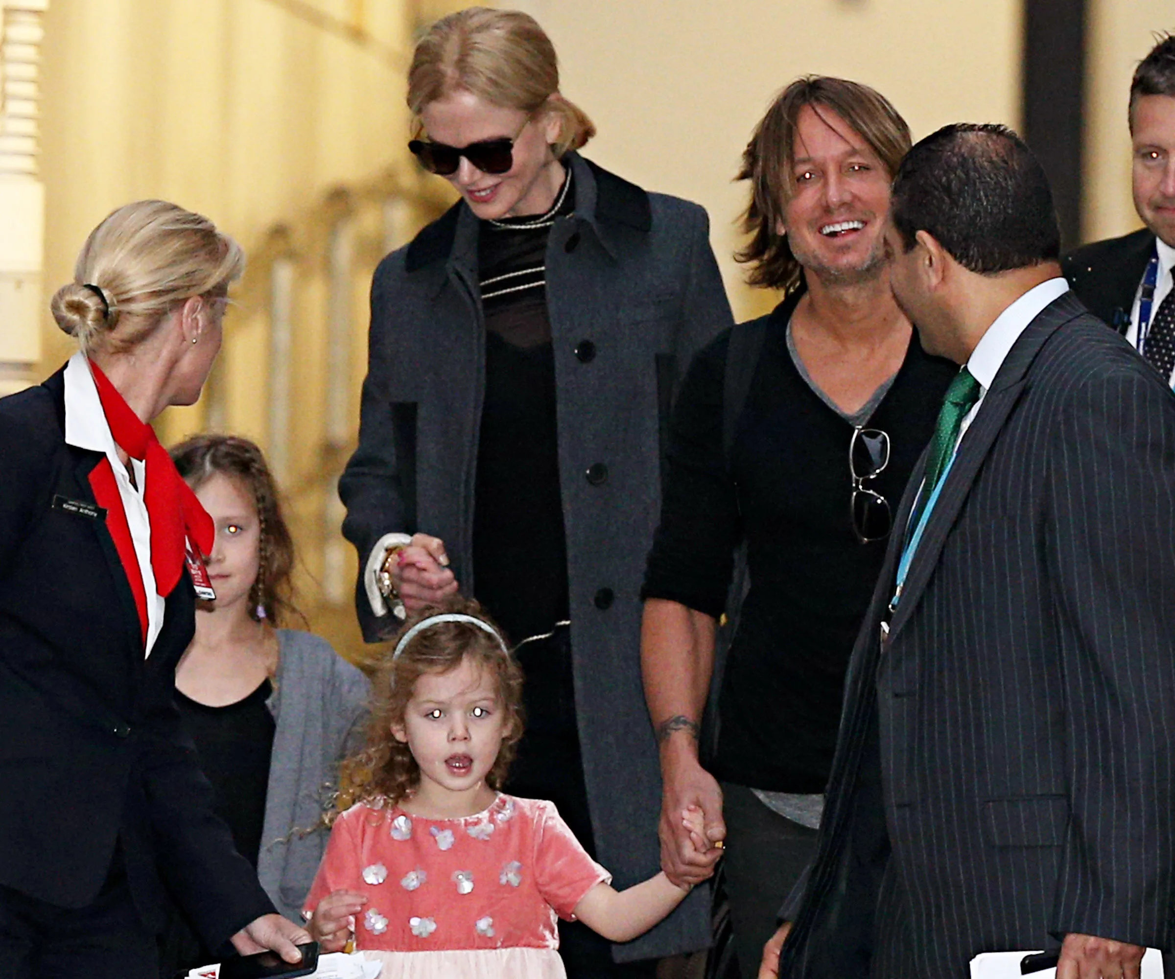 People arriving at an airport, smiling and holding hands, with an airline staff member assisting.