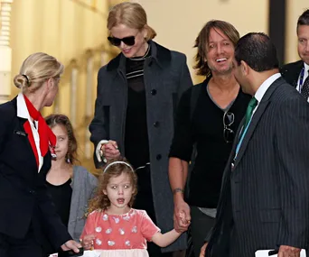 People arriving at an airport, smiling and holding hands, with an airline staff member assisting.