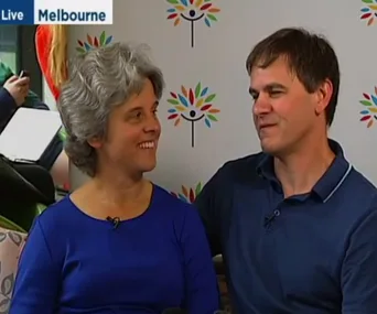 A couple sits together, smiling, during a live broadcast in Melbourne.