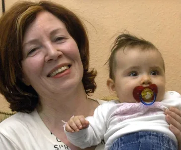 Smiling woman holding a baby with a pacifier, both appear happy and relaxed.