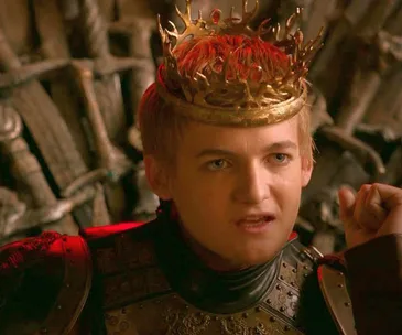 King Joffrey from Game of Thrones wearing a crown, looking serious, in front of the Iron Throne.