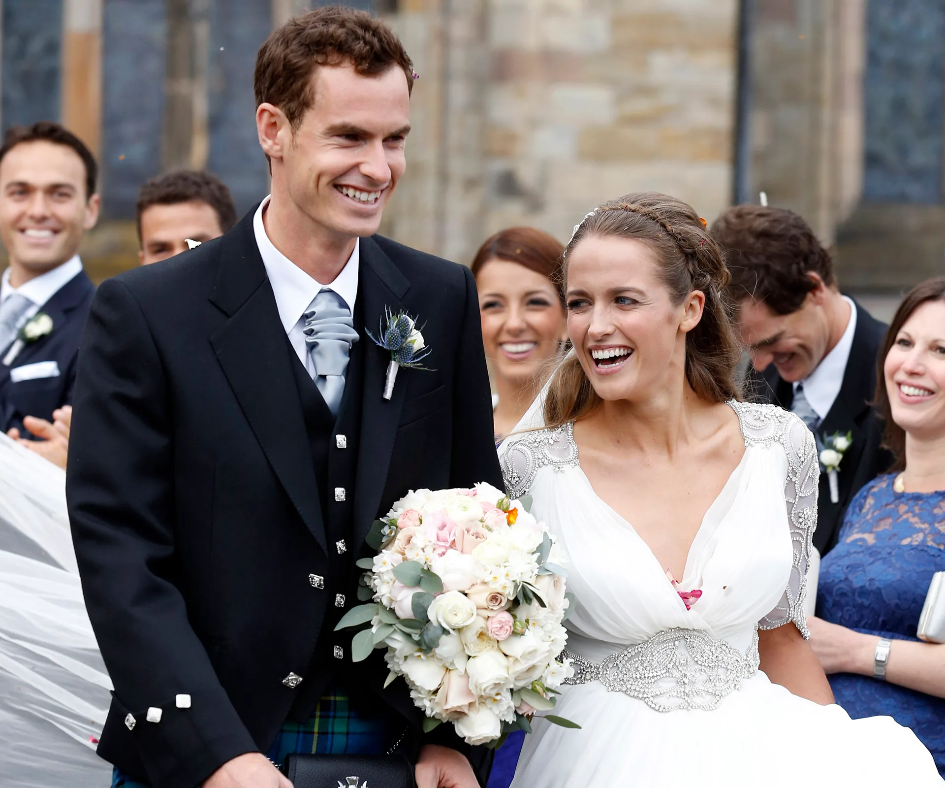 A happy couple celebrating their wedding, surrounded by smiling guests, with the bride in a white dress holding a bouquet.