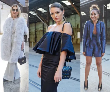 Three women in diverse, stylish outfits at a fashion event; one in fur, one in off-shoulder dress, one in a blue suit.