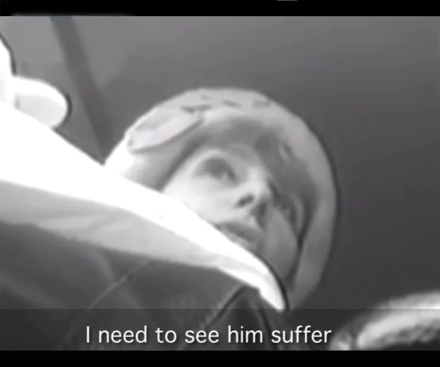 A person in a winter hat captured in a low-angle grayscale surveillance image with subtitles: "I need to see him suffer."