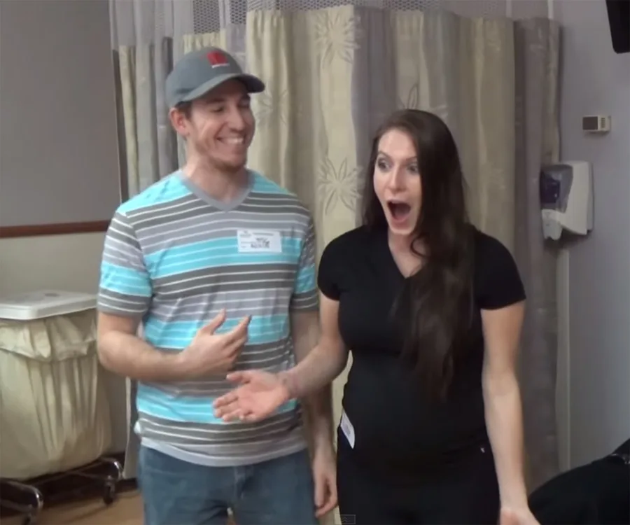 Couple in a hospital room look surprised and delighted, with woman holding her mouth open in shock and excitement.