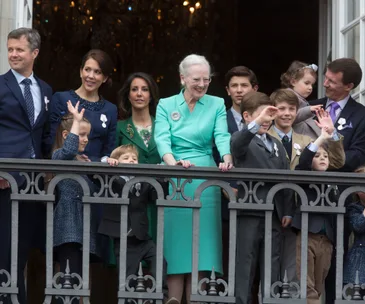 Royal family gathered on a balcony celebrating Queen Margrethe’s birthday, smiling and waving at the crowd.