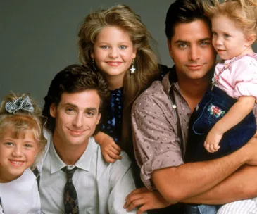 A group photo of five smiling characters from the TV show "Full House," showcasing family bonding and joy.