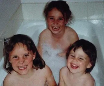 Three smiling children in a bathtub playing with bubbles.