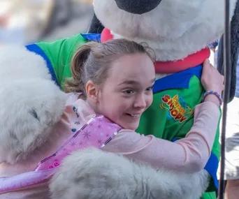 Girl happily hugs a large Snoopy mascot at a birthday event.