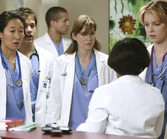 Doctors in white coats gather around a table, engaged in a serious discussion.