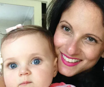 A smiling woman and baby with blue eyes, the baby wearing a pink bow in her hair.