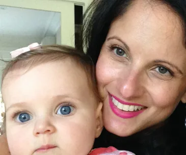 A smiling woman and baby with blue eyes, the baby wearing a pink bow in her hair.