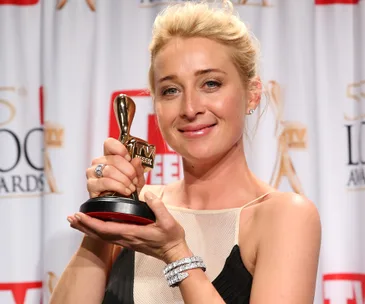 A woman holding a Logie Award, smiling, in front of a red and white backdrop at a TV event.