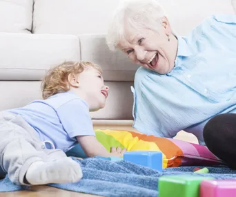 Grandmother and young child laughing together while playing on the floor with colorful toys.