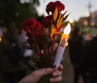 A person holding red flowers and an Amnesty International candle during a vigil at dusk.