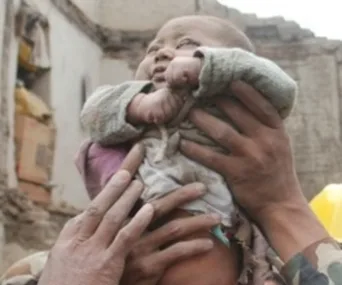 Rescuer lifts a baby boy from earthquake rubble in Nepal; the child looks safe in protective hands.