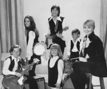 A black and white image of "The Partridge Family" cast playing musical instruments in matching outfits.