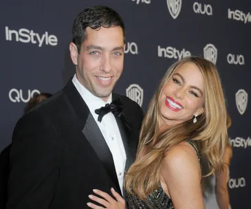 A smiling couple poses at a formal event, with the woman in a black dress and the man in a tuxedo.