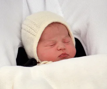 A newborn baby bundled in a white knit hat and blanket, peacefully sleeping.