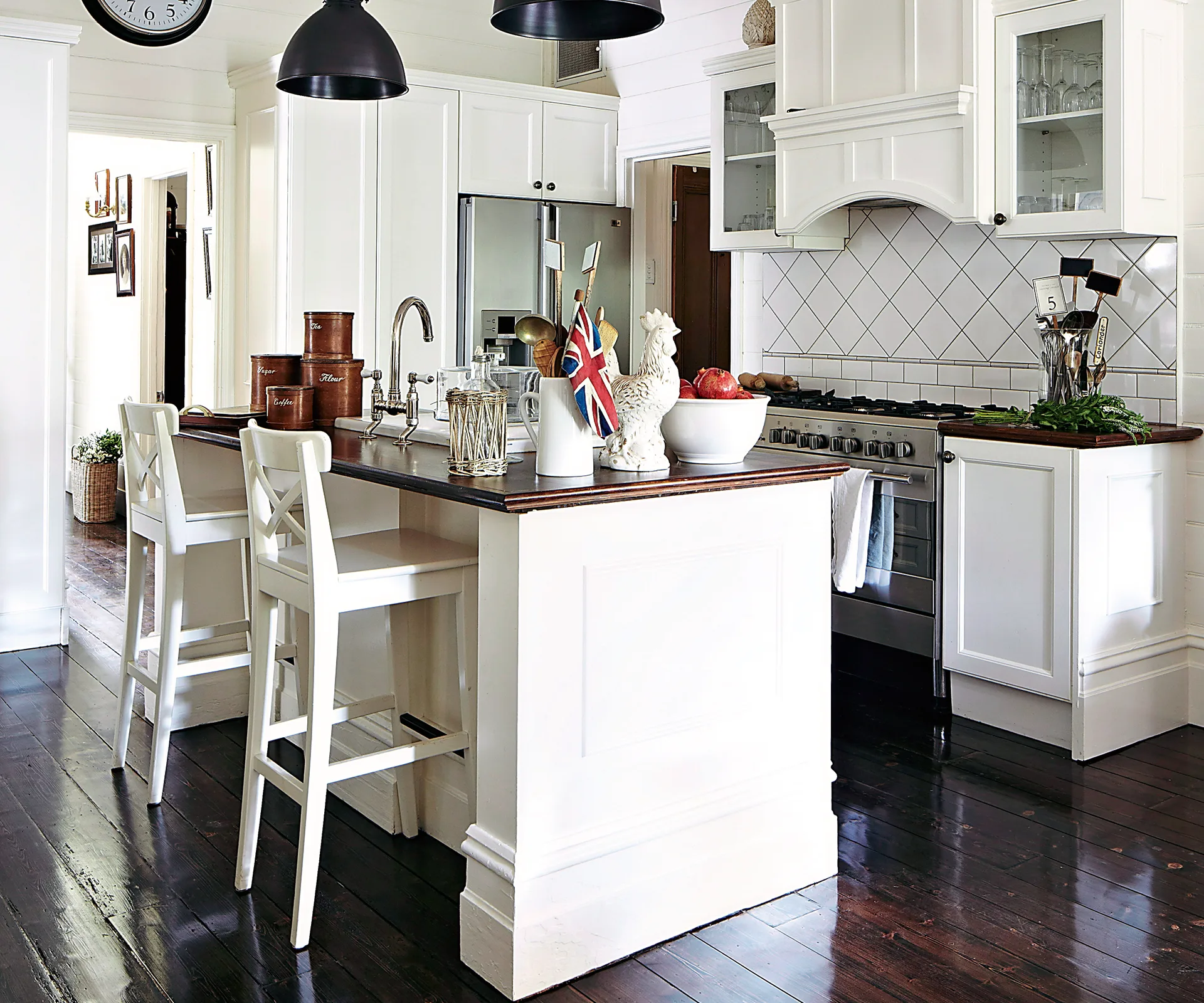 Alt text: "Modern kitchen with white cabinets, dark wood floor, island, bar stools, and decor items like flag and vases."