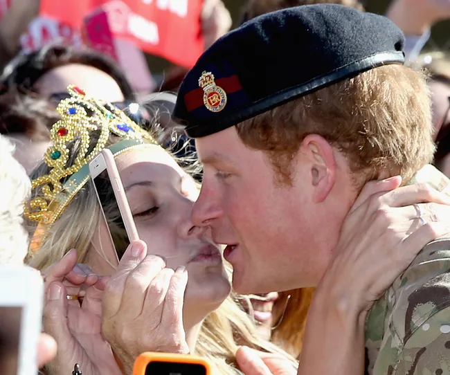 A man in military attire kisses a woman wearing a jeweled crown among a crowd.