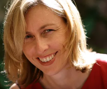Smiling woman with blonde hair in a red top, outdoors in natural light.