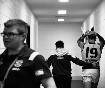 A player wearing jersey 19 walking down a hallway with a person, depicted in a candid, supportive moment.