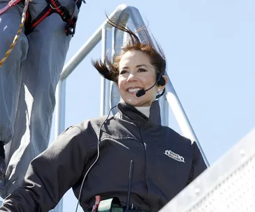 Woman smiling while wearing a headset and harness, hair blowing in the wind on a bridge climb.