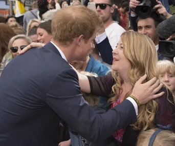 A person in a suit greeting a woman in a crowd, surrounded by people taking photos and videos.