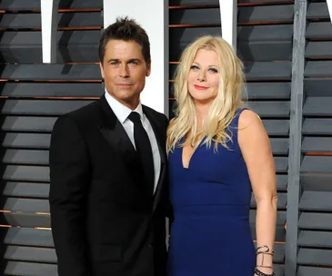 A man in a suit and a woman in a blue dress smiling at an event with striped background.