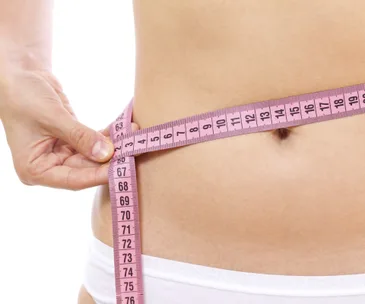 "Close-up of a person measuring their waist with a pink tape measure."