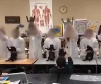 Students in lab coats wave taxidermy cats in a classroom, with anatomy posters on the wall.