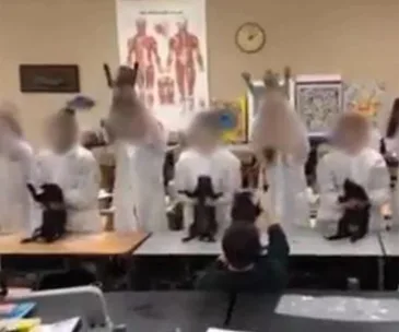 Students in lab coats wave taxidermy cats in a classroom, with anatomy posters on the wall.