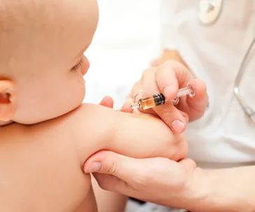 A healthcare professional administers an injection to an infant's arm.