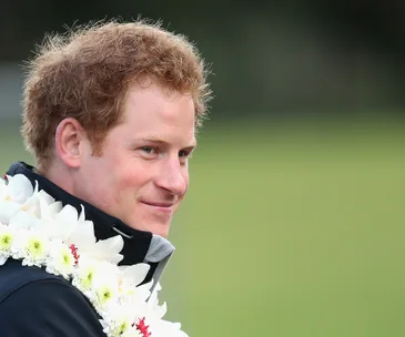 A person wearing a floral lei smiles while looking to the side, set against a grassy background.