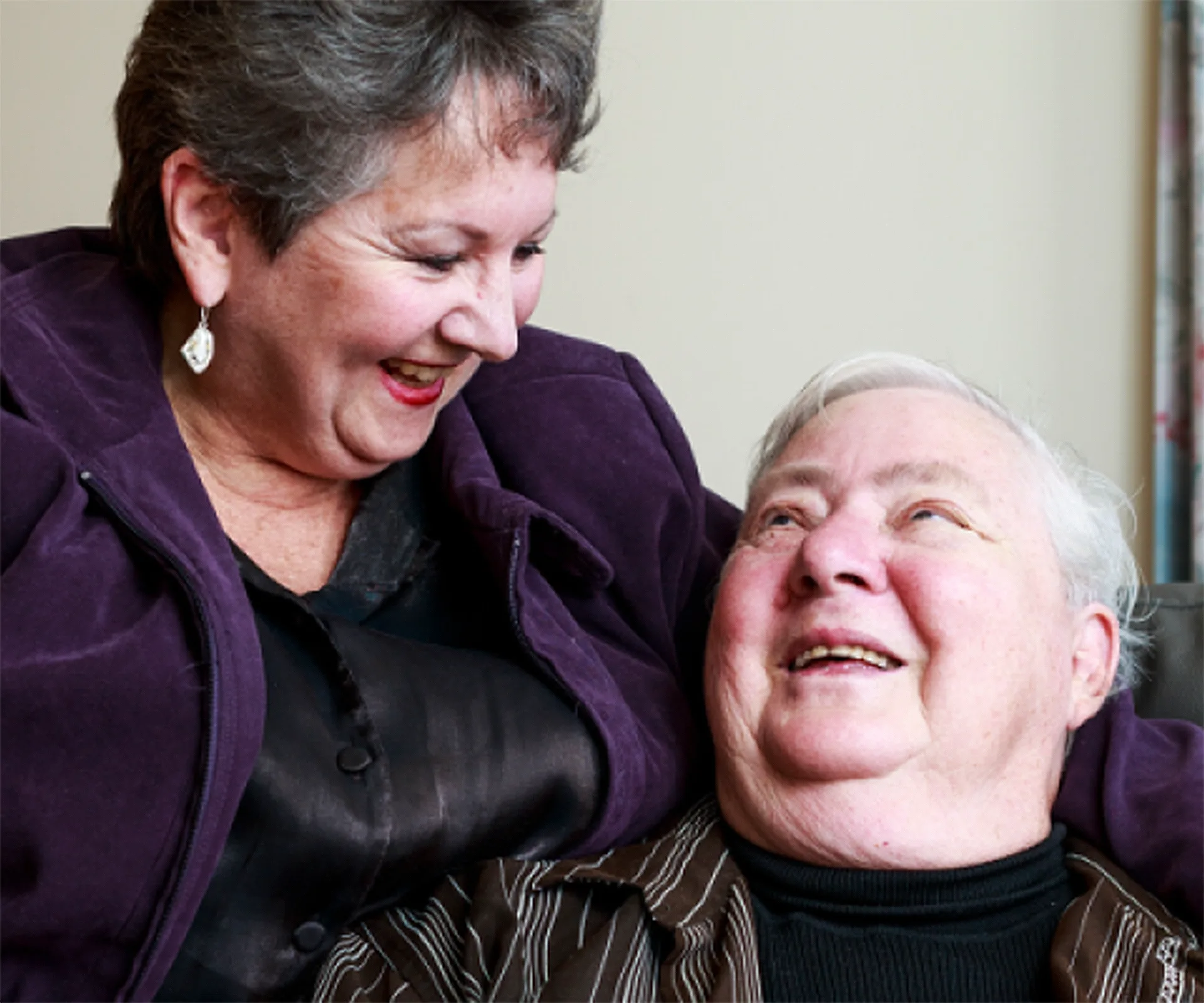 An elderly couple smiles warmly at each other, radiating joy and affection in a candid moment together.