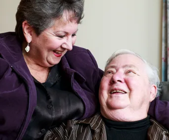 An elderly couple smiles warmly at each other, radiating joy and affection in a candid moment together.