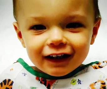 A smiling toddler wearing a hospital gown with playful animal prints.