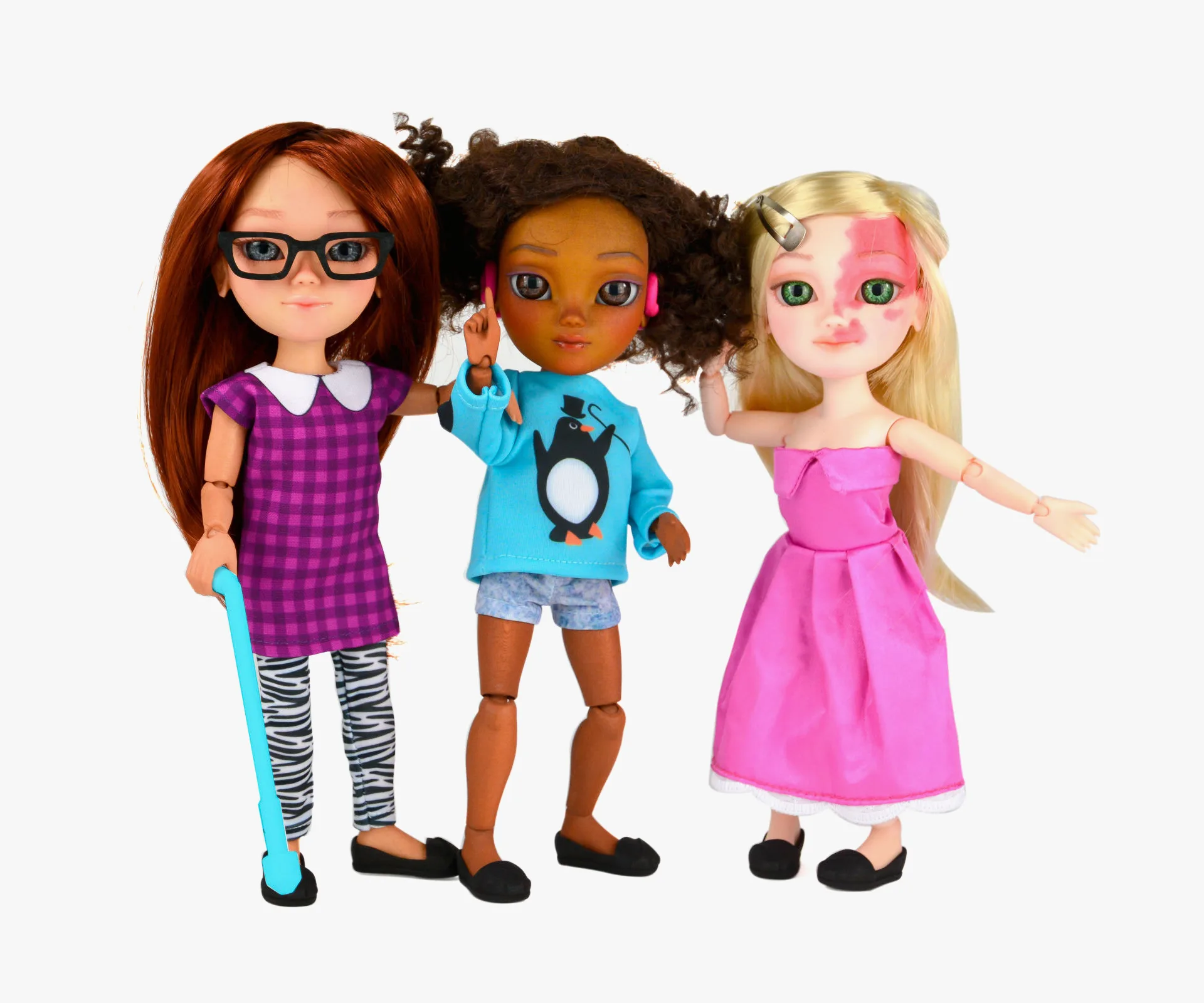 Three diverse dolls: one with glasses and a cane, another with arm prosthetic, and one with a birthmark, all smiling.