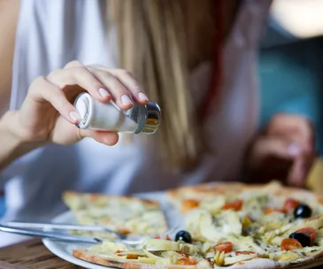 Person adding salt to a pizza slice on a plate.