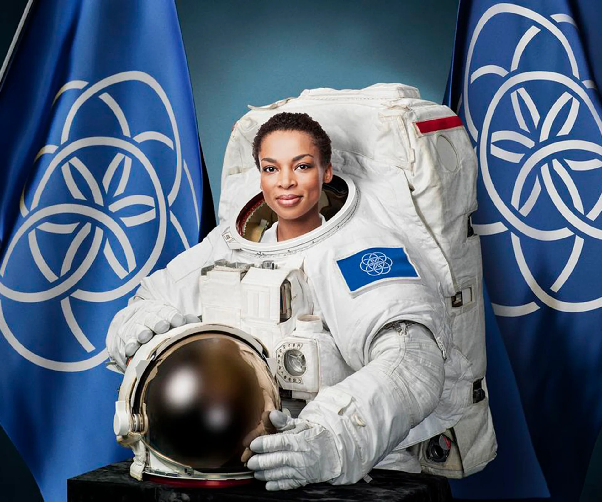 Astronaut in spacesuit with Earth flag, standing between two Earth flags, holding helmet.