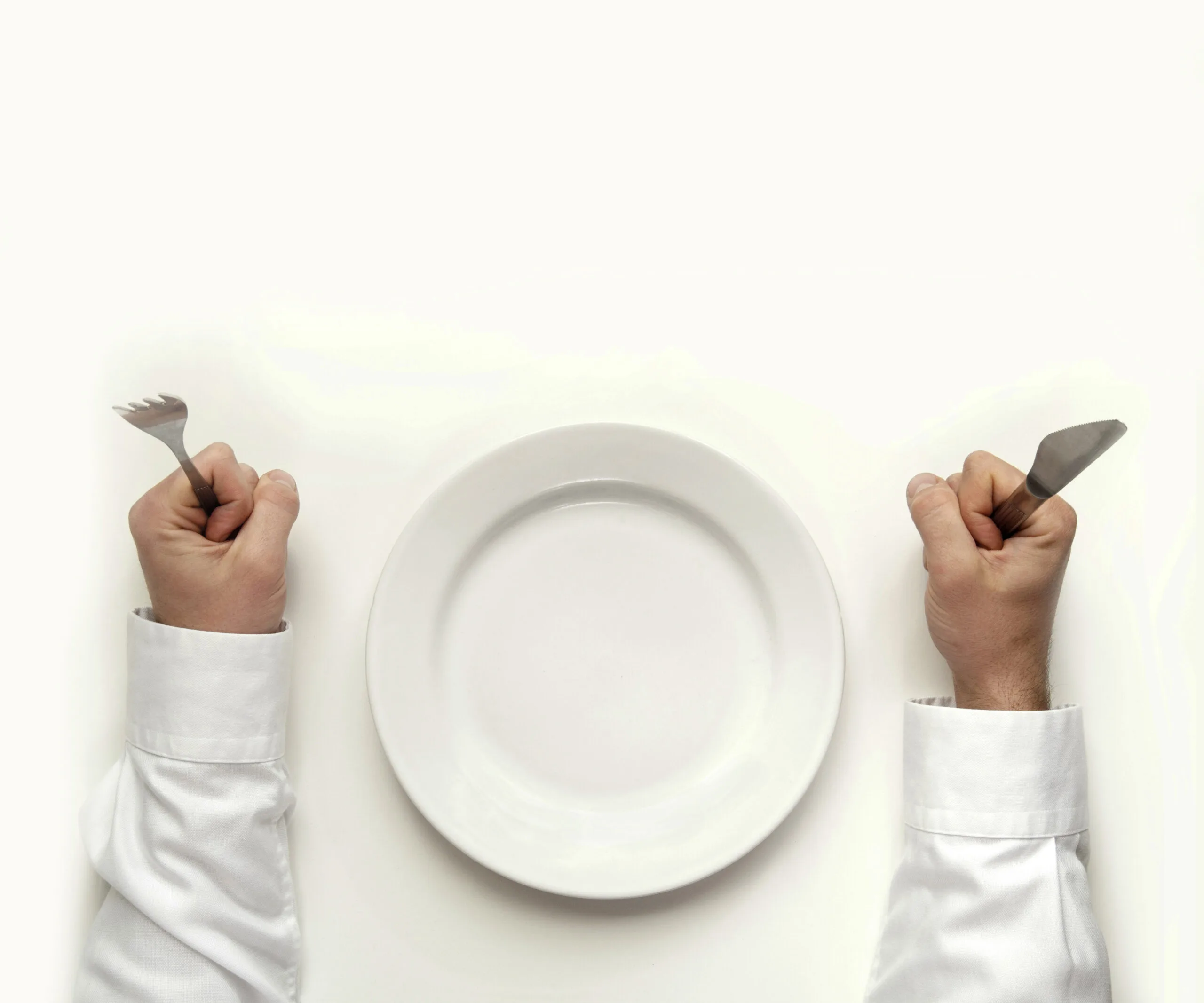 Empty plate with hands holding fork and knife, symbolizing hunger or skipped meals.