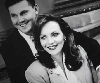 A black and white photo of a smiling couple, with the woman in front and the man slightly behind her.