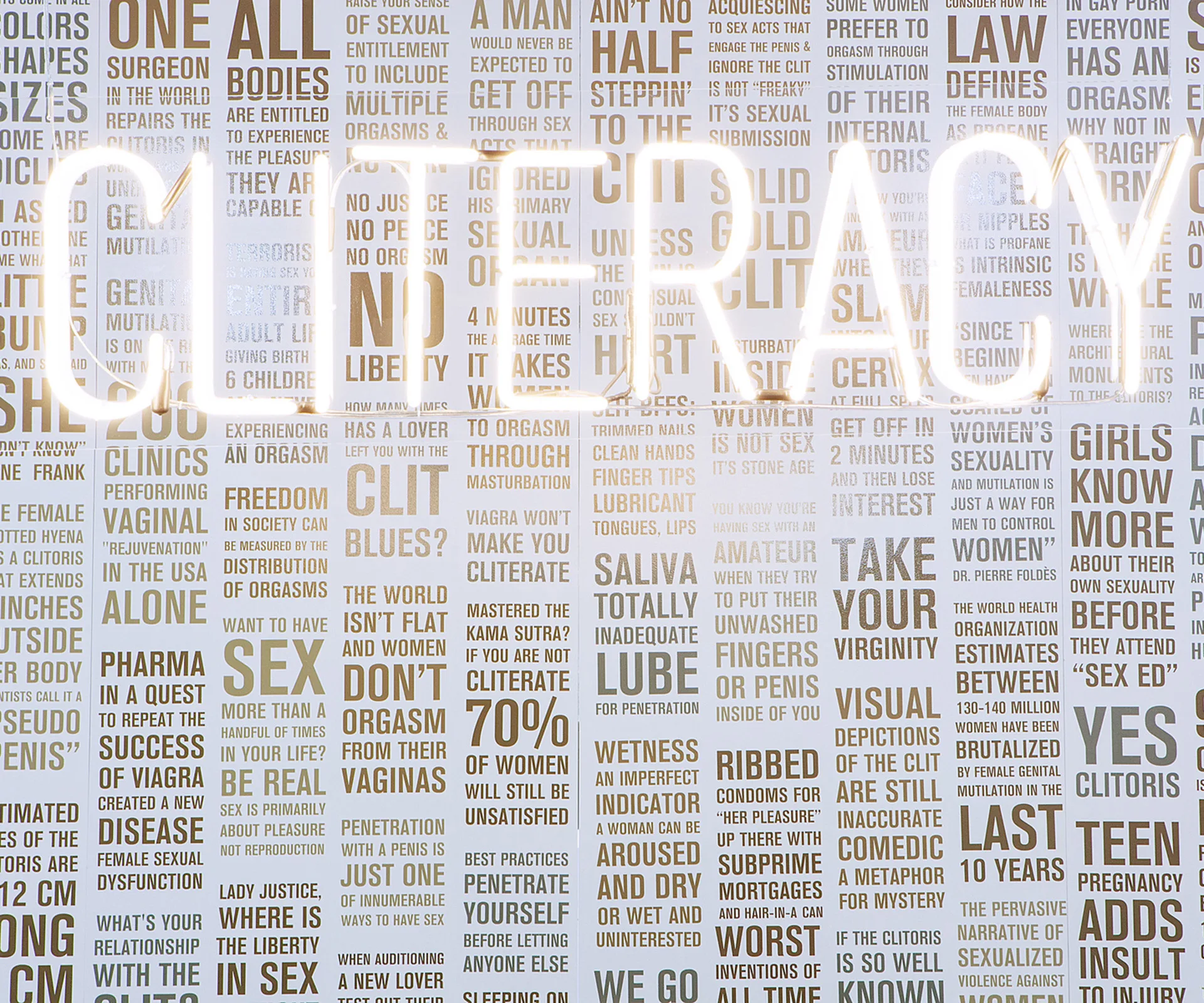 Neon "CLITERACY" sign overlaid on a wall with text about women's sexual health and rights.