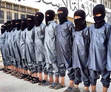 A line of children wearing black uniforms and masks stand against a wall with Arabic writing.