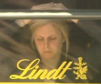 A person behind a window with "Lindt" written, appearing thoughtful or concerned inside the cafe.